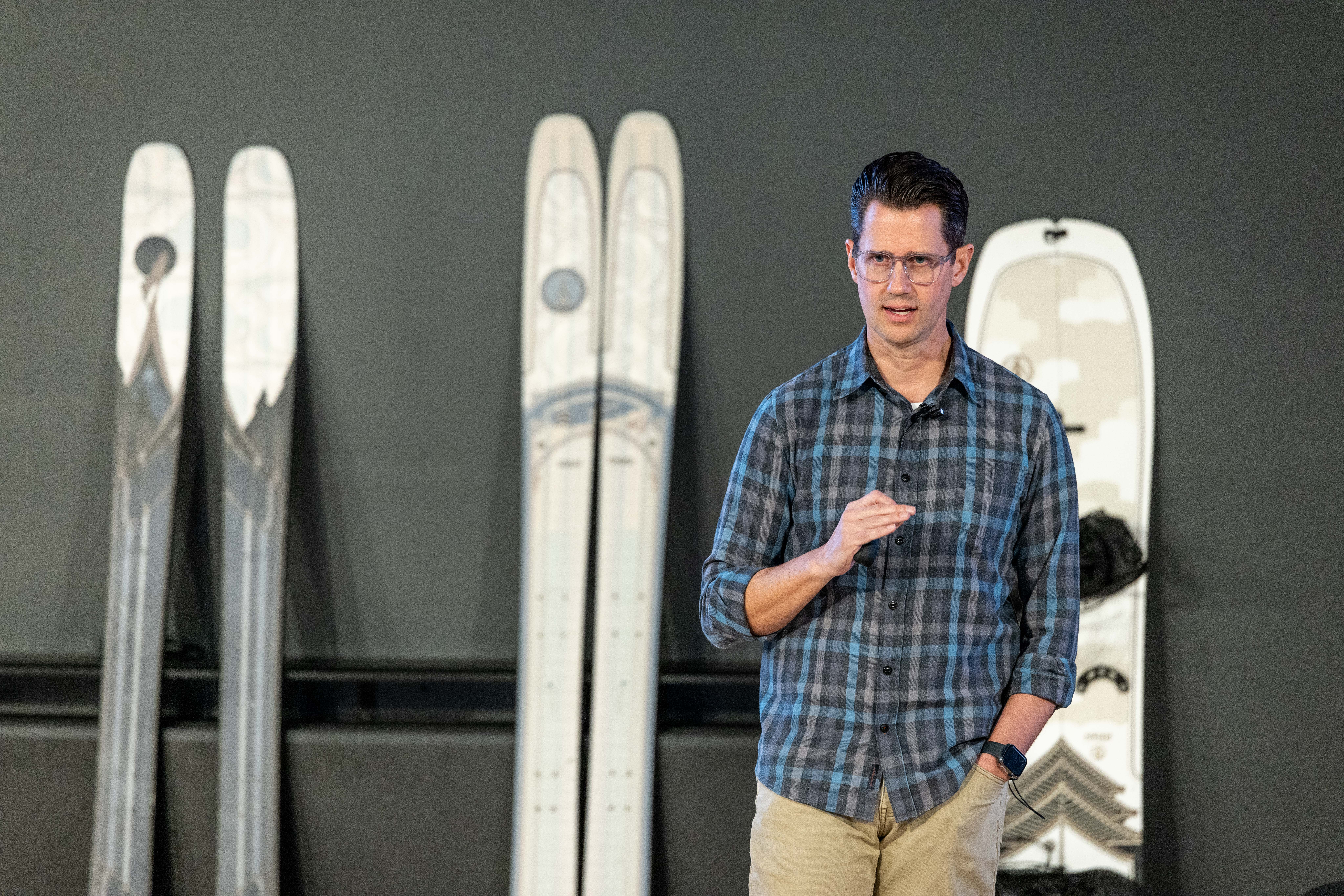 Tanner Bell speaking at Utah Valley University, with snowboards and skis displayed behind him