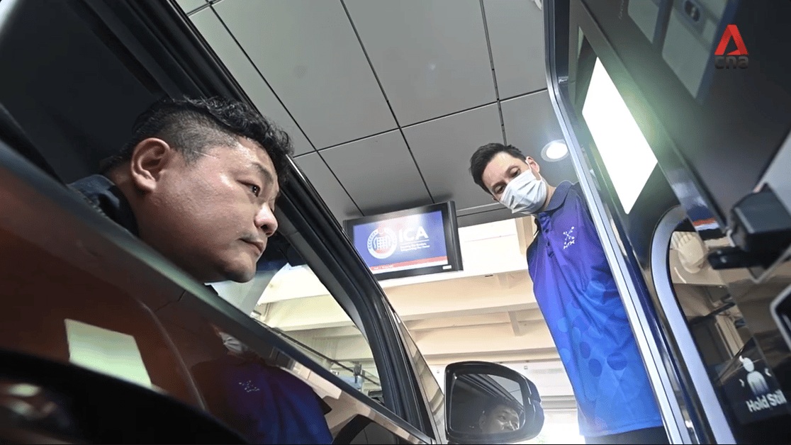 A driver uses a Tascent biometric scanner at Singapore's Woodlands Checkpoint while an officer observes.