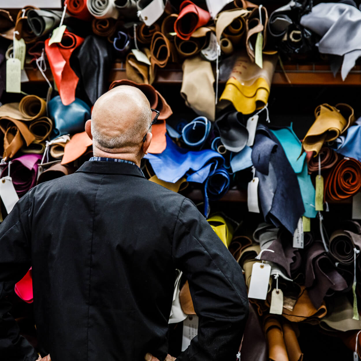 A person examining shelves of rolled, brightly colored leather