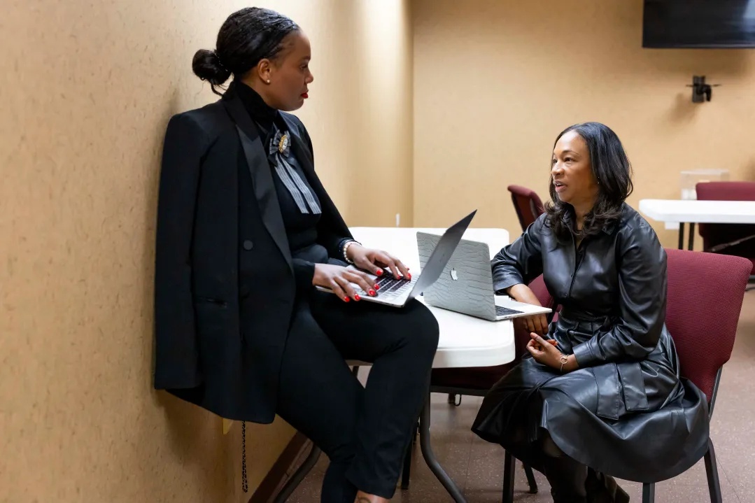Two women working with laptops at a table in a meeting room, in a photograph accompanying coverage of Jesse Jackson memorial preparations.
