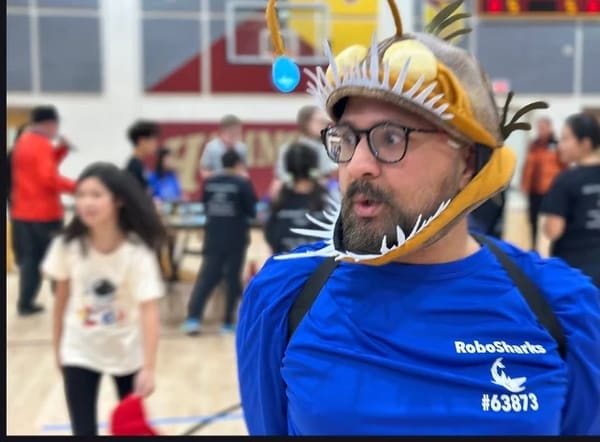 Tarun Upaday wearing a shark costume over a blue RoboSharks shirt at a robotics gathering