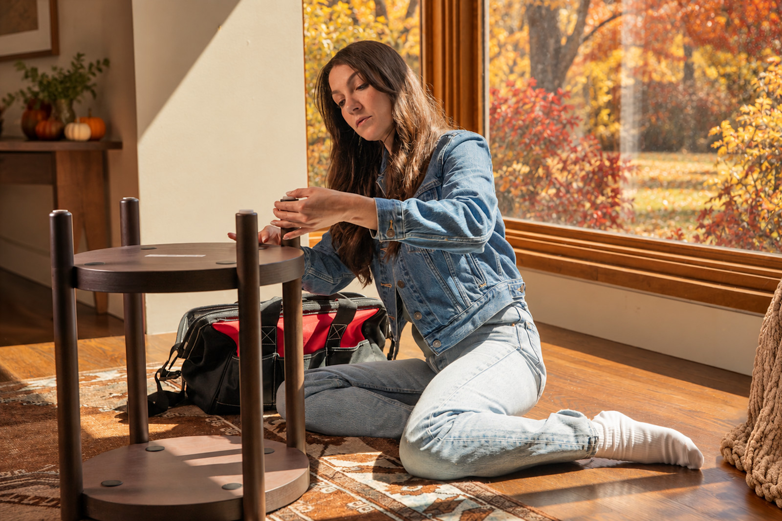 A Tasker assembling a table beside a tool bag in a sunlit room