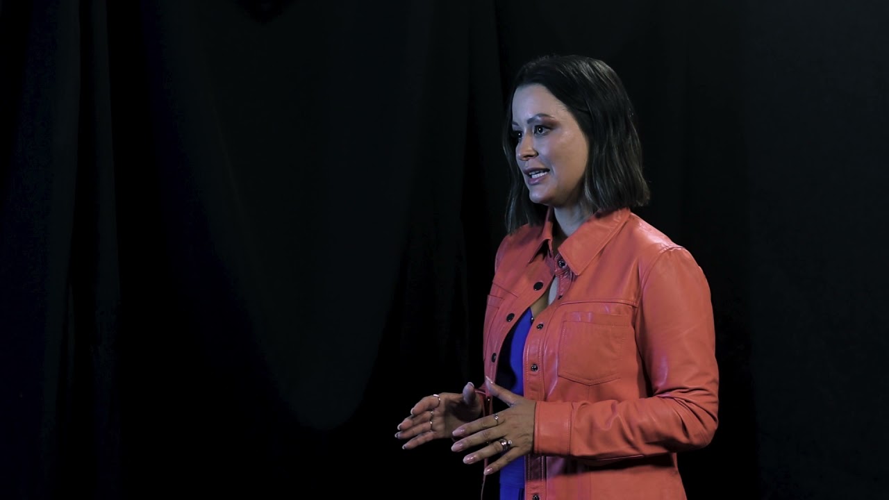 Tatiane Vita speaking on the TEDxBeloHorizonte stage in an orange jacket