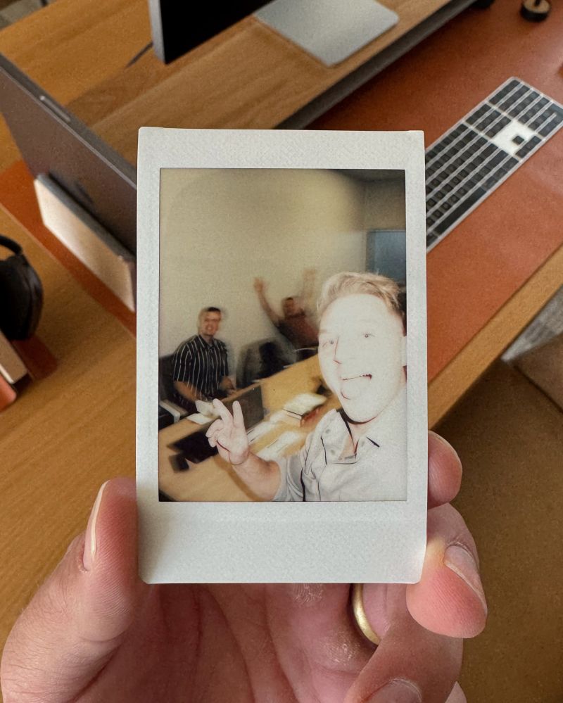 An instant photograph of an early office scene held above a laptop