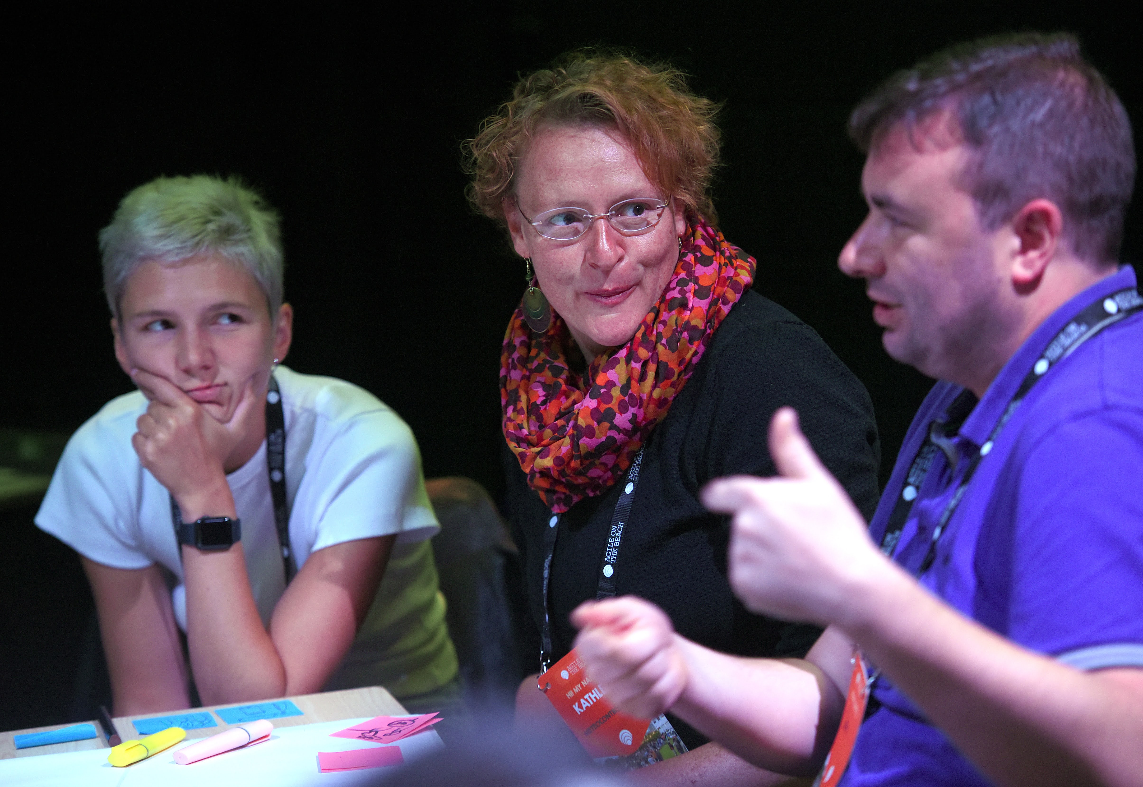 Three participants exchanging ideas around a table at Agile on the Beach
