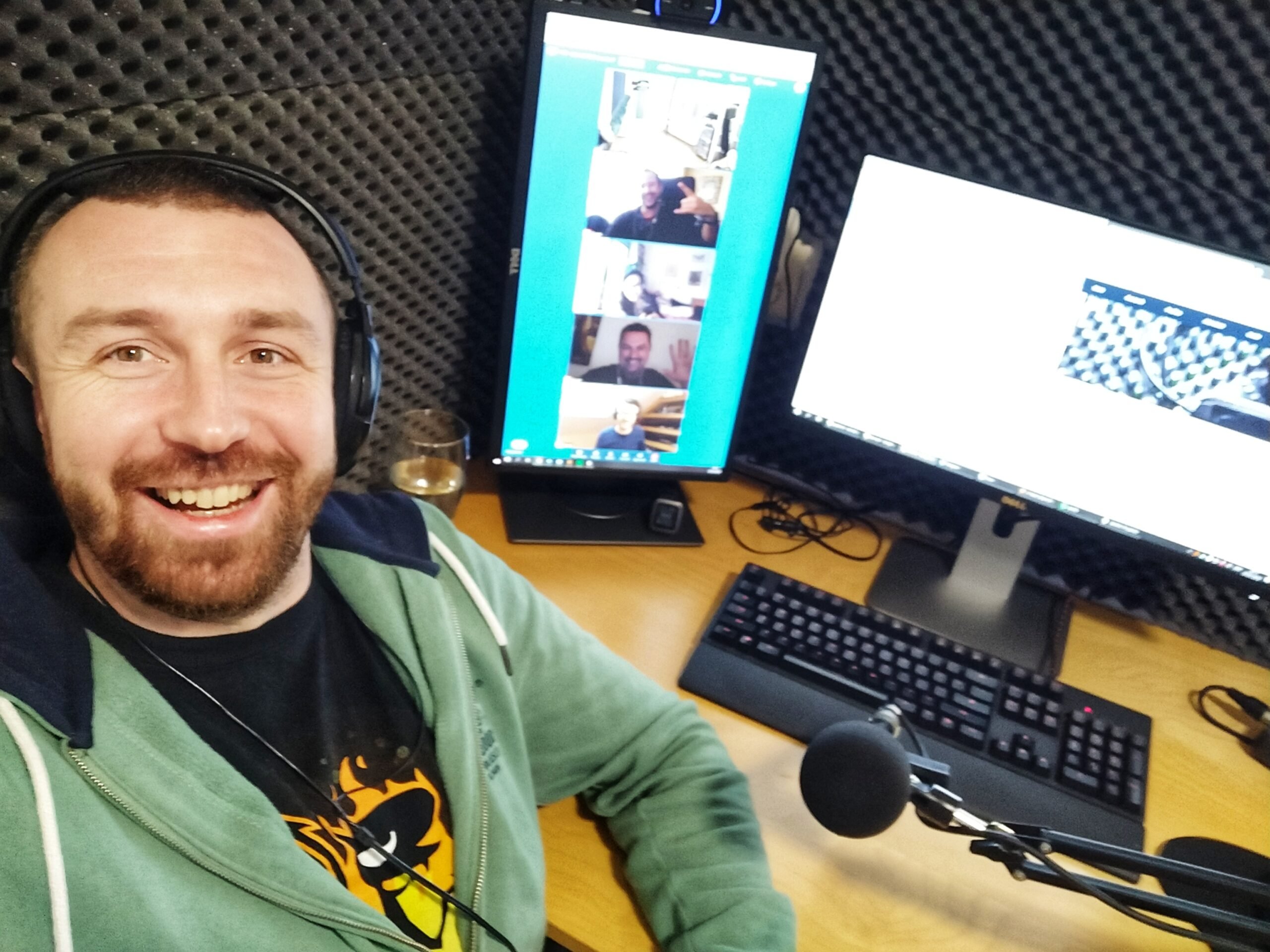 A headphone-wearing podcaster beside a microphone and monitors showing remote participants in the episode 100 recording