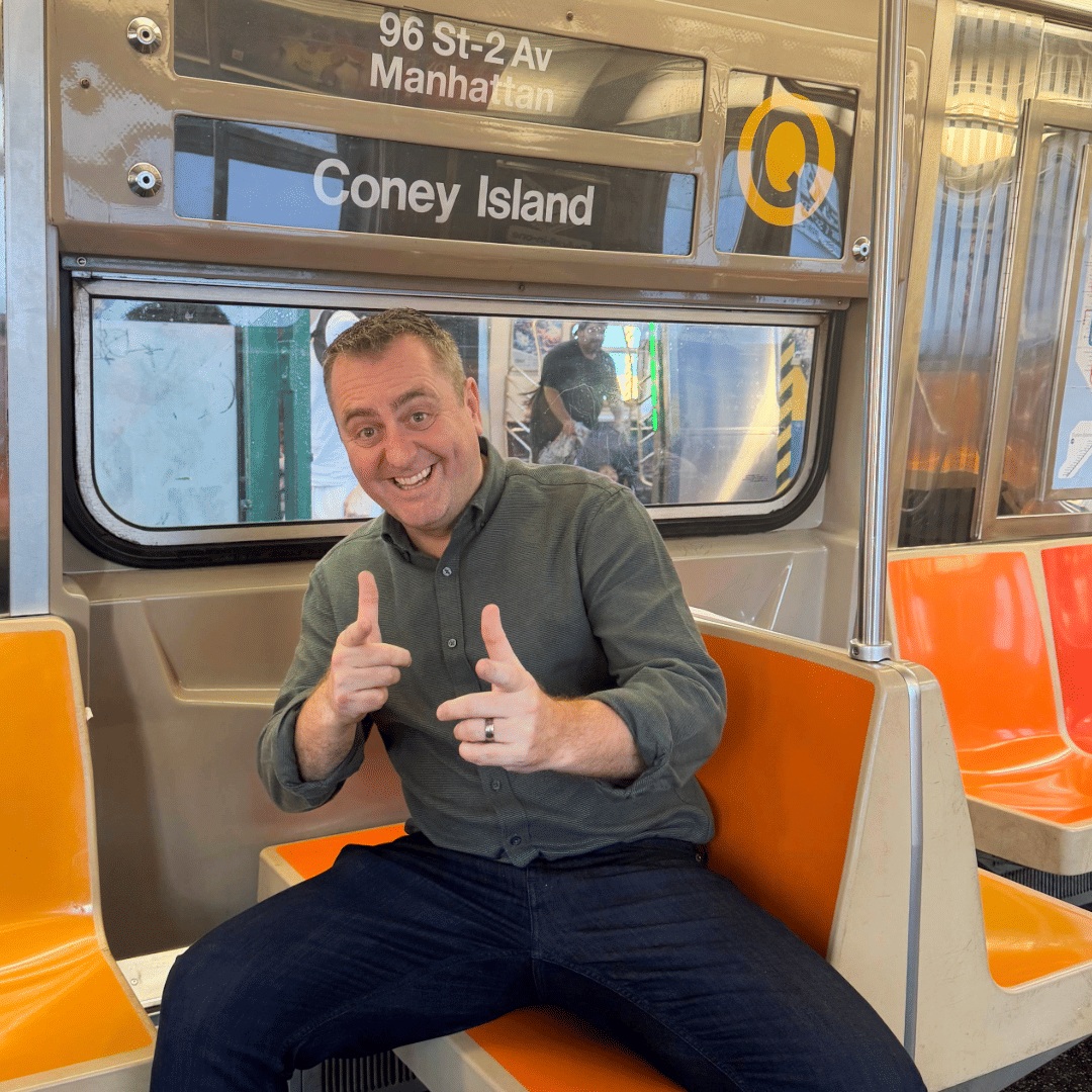 Neil C. Hughes smiling on a New York subway train