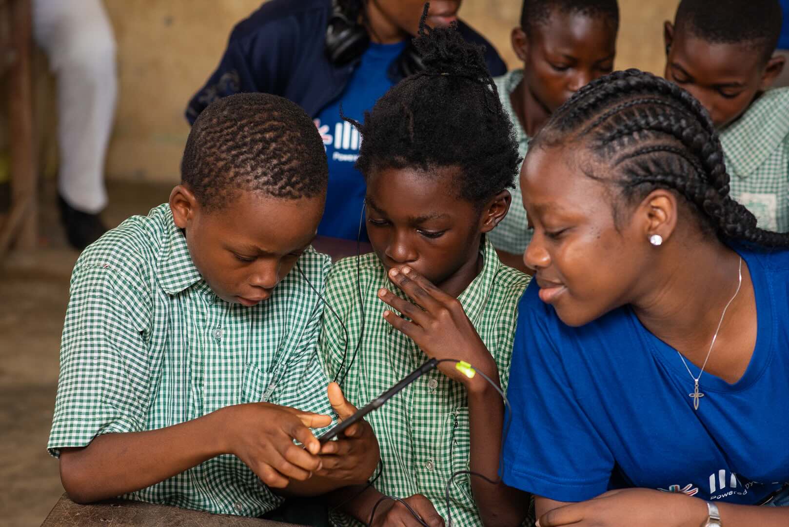 School-age learners and a facilitator looking at a mobile phone during a Tech4Dev activity