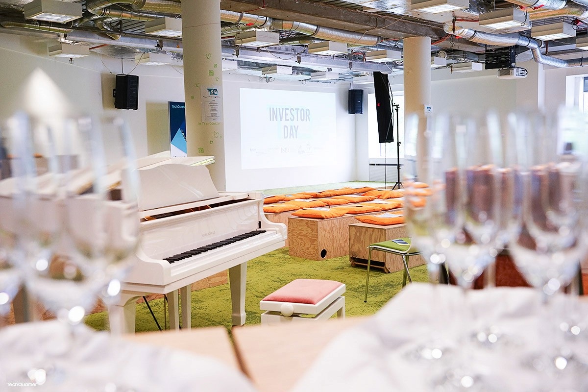 TechQuartier event space with a white piano, seating and an Investor Day projection