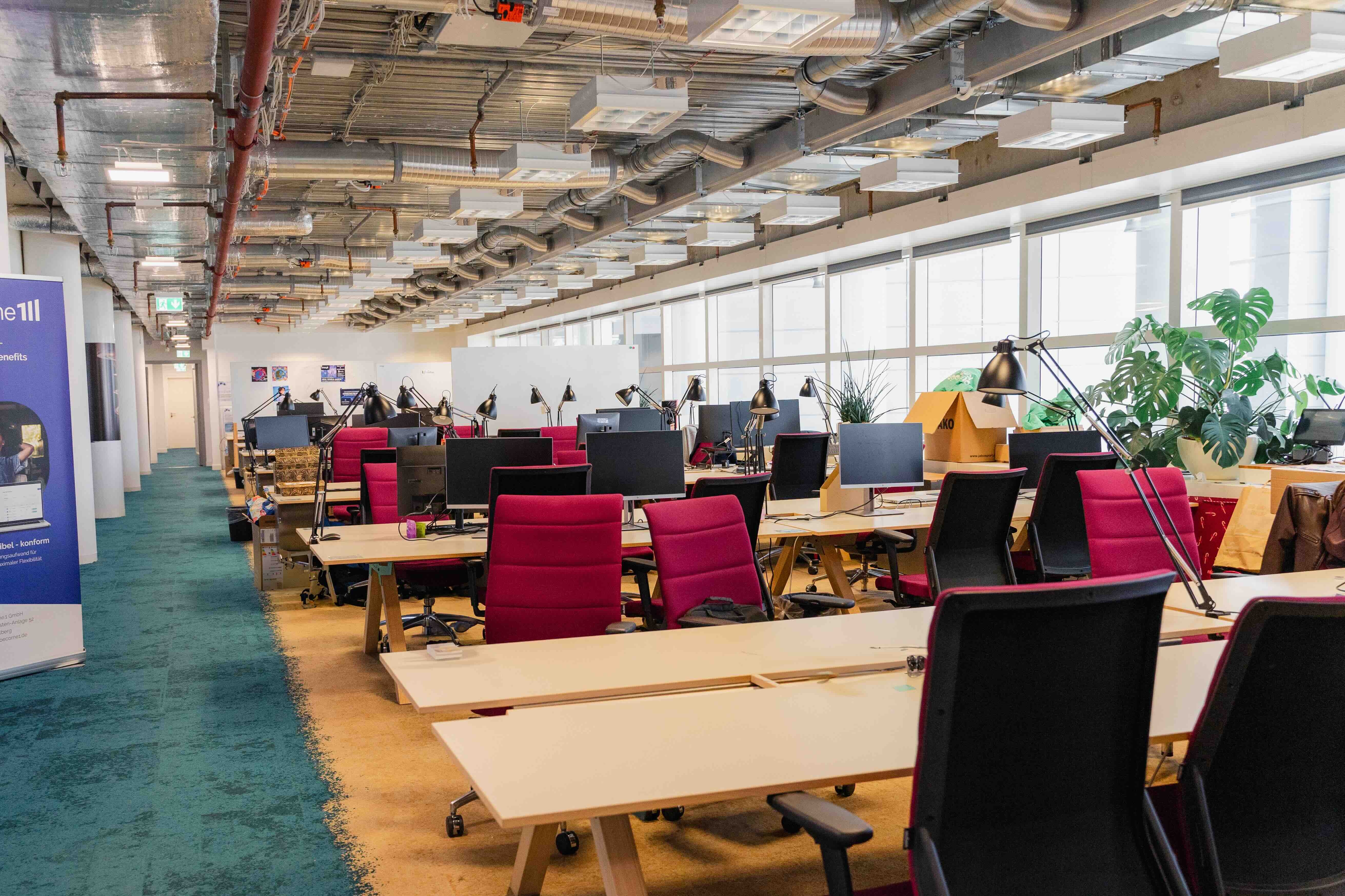 Rows of desks, red office chairs and plants in TechQuartier’s Frankfurt coworking space