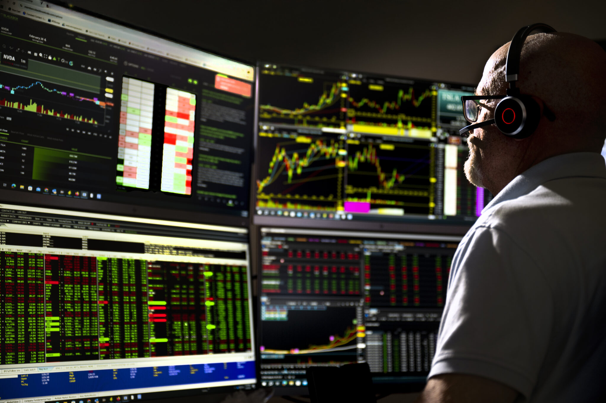 A headset-wearing financial professional watches market data across several trading monitors