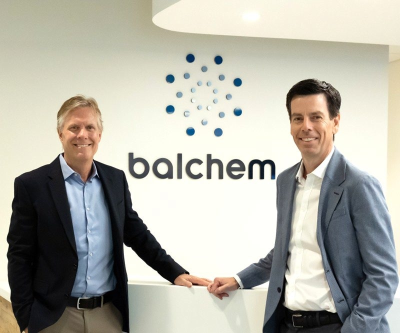 Ted Harris, left, and Martin Bengtsson standing beside the Balchem logo in an office lobby