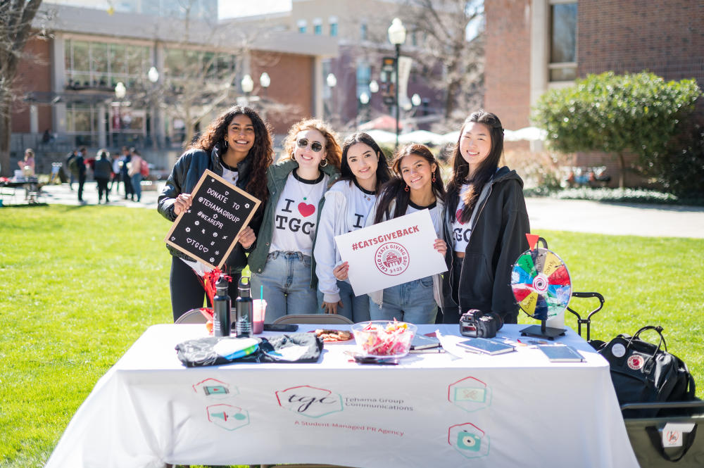 Five students pose at a Tehama Group Communications fundraising table on the Chico State campus