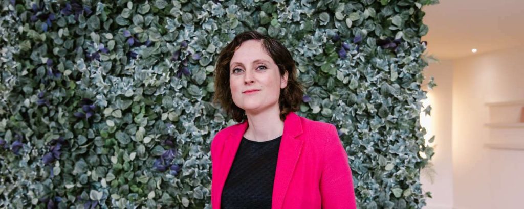 Tekkoo co-founder Lindy Hensen in a pink jacket beside a wall of foliage
