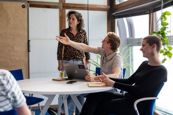 Tekkoo colleagues discussing work around a table with a whiteboard
