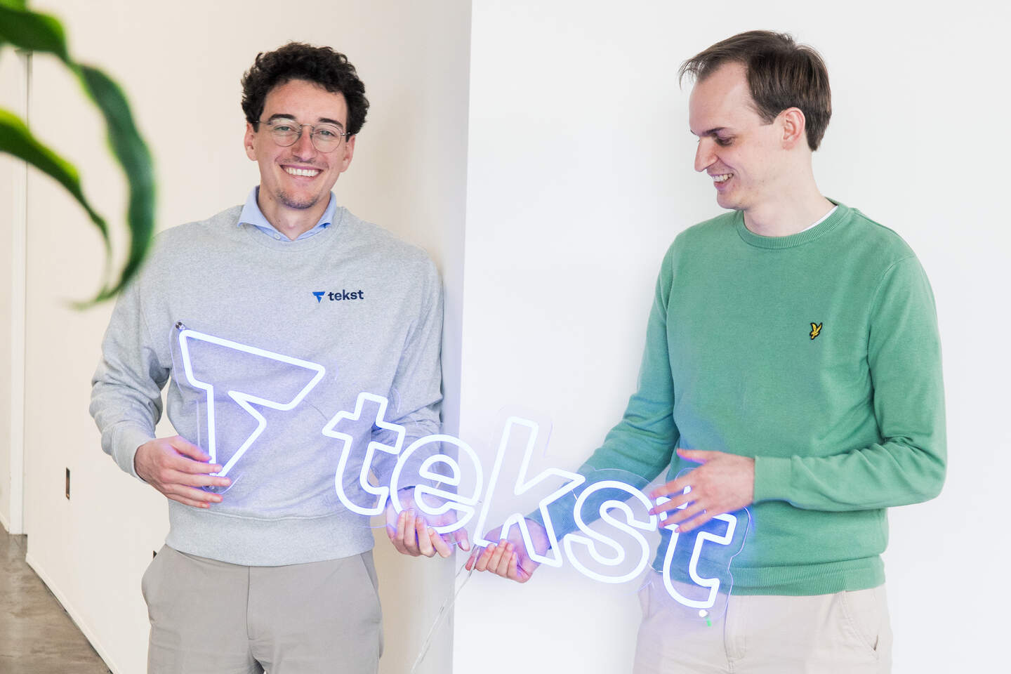 Tekst’s two co-founders holding an illuminated company sign