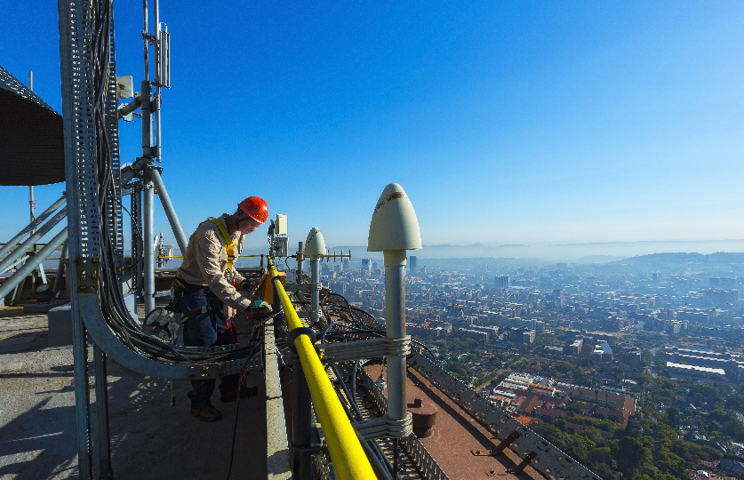 A technician works beside telecommunications equipment high above a South African city