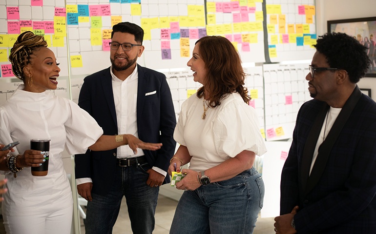 Teneshia Jackson Warner, at left, in conversation with a group in front of a wall covered in colorful notes.