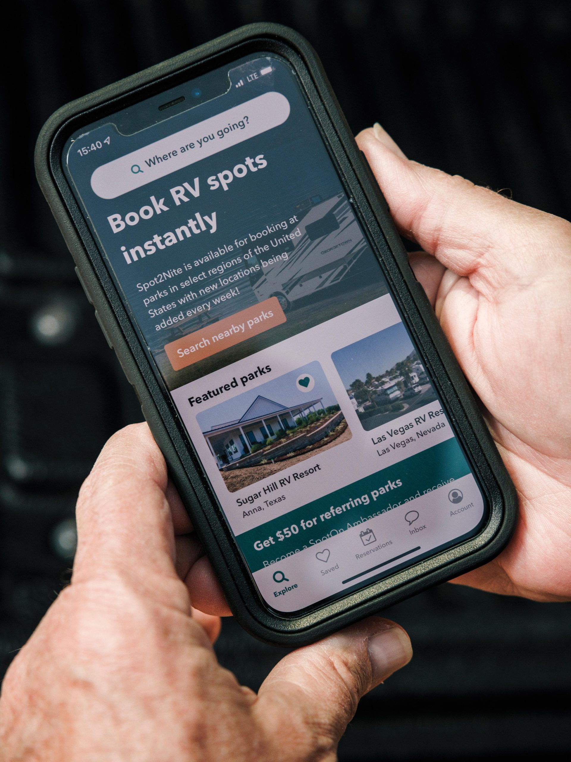 Hands holding a phone displaying the Spot2Nite instant RV-site booking screen