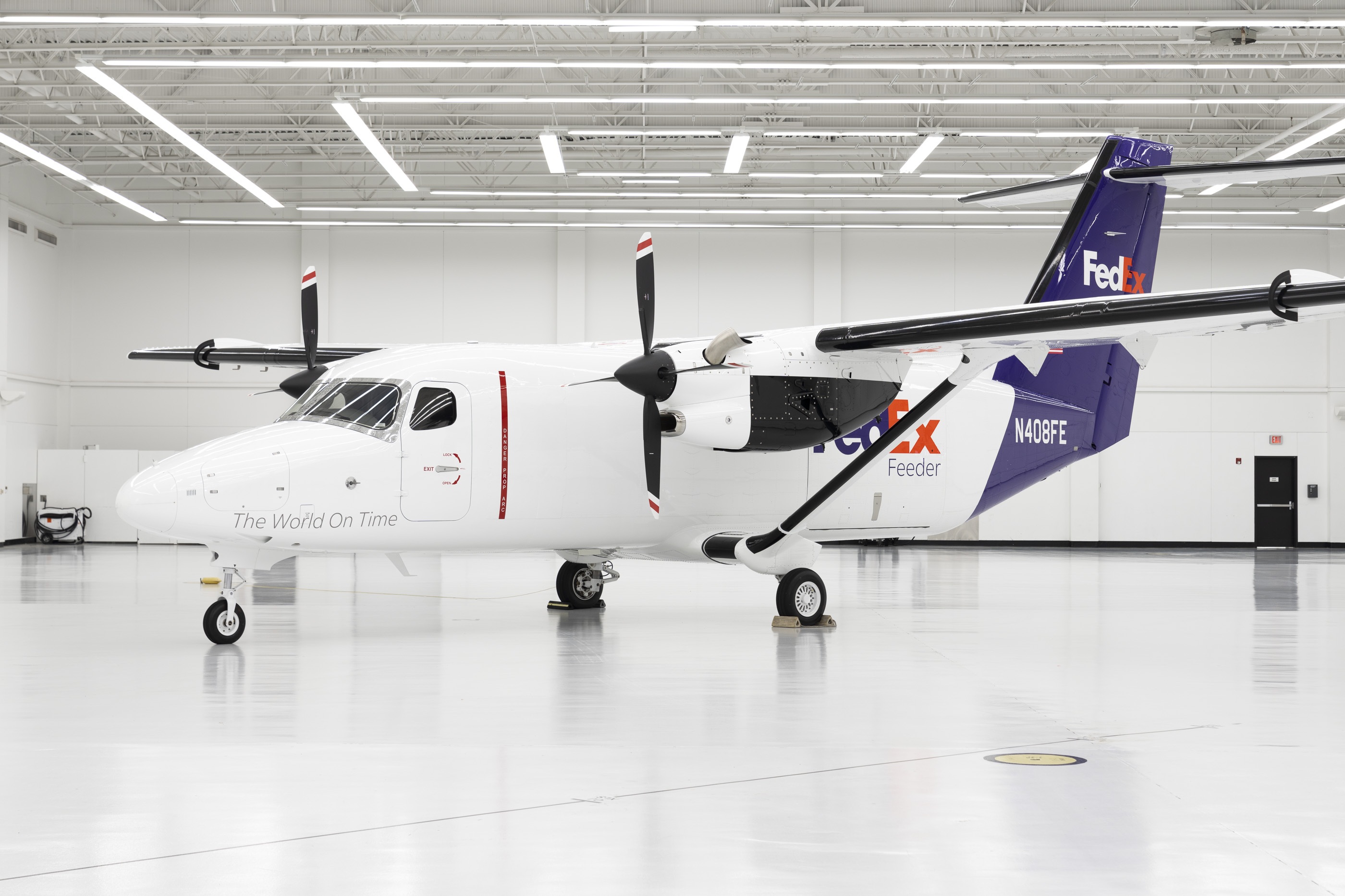 A white and purple FedEx Cessna SkyCourier parked inside a brightly lit hangar