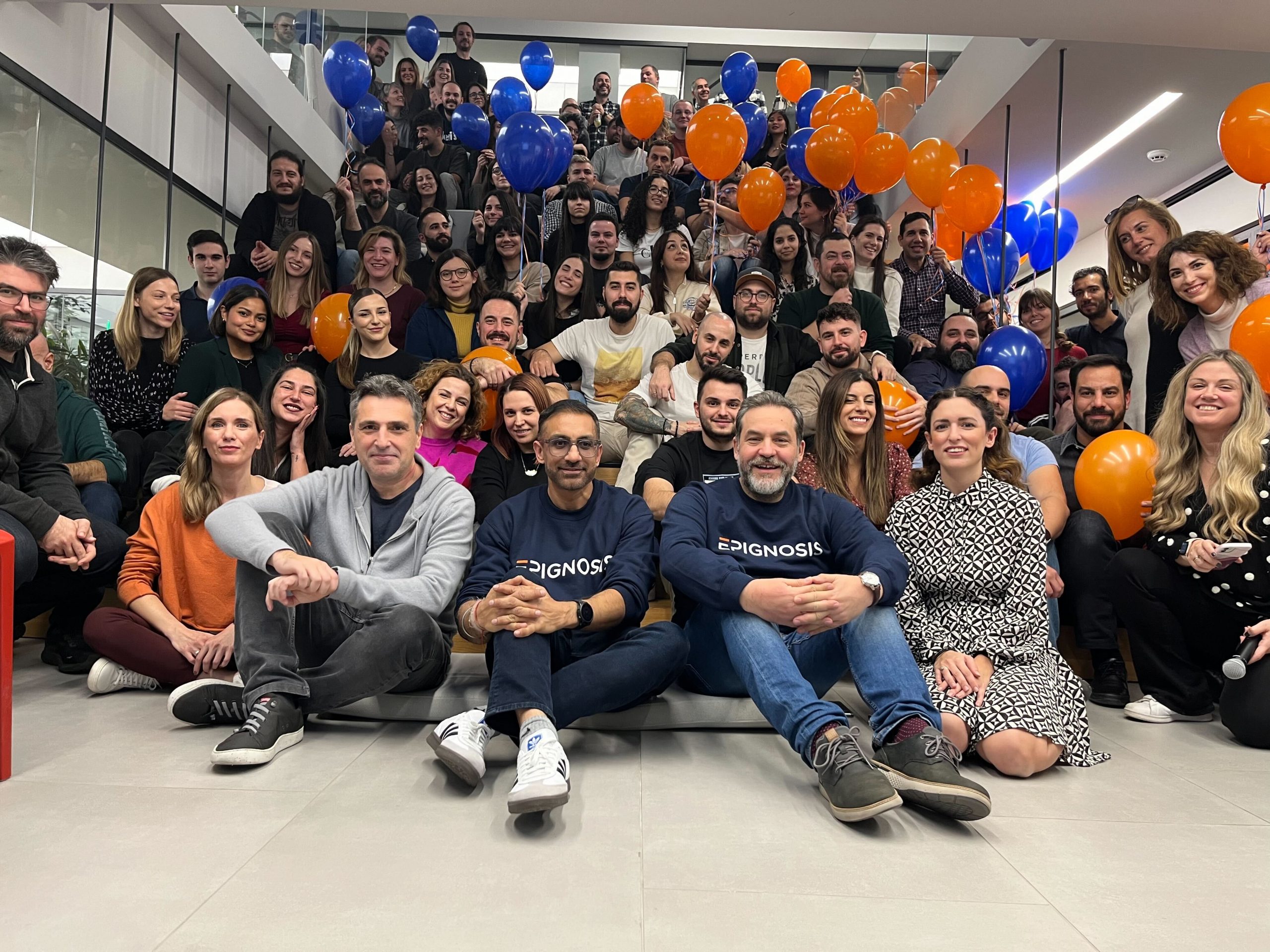 Thanos Papangelis, Nikhil Arora and Dimitris Tsingos seated with Epignosis colleagues on an office staircase