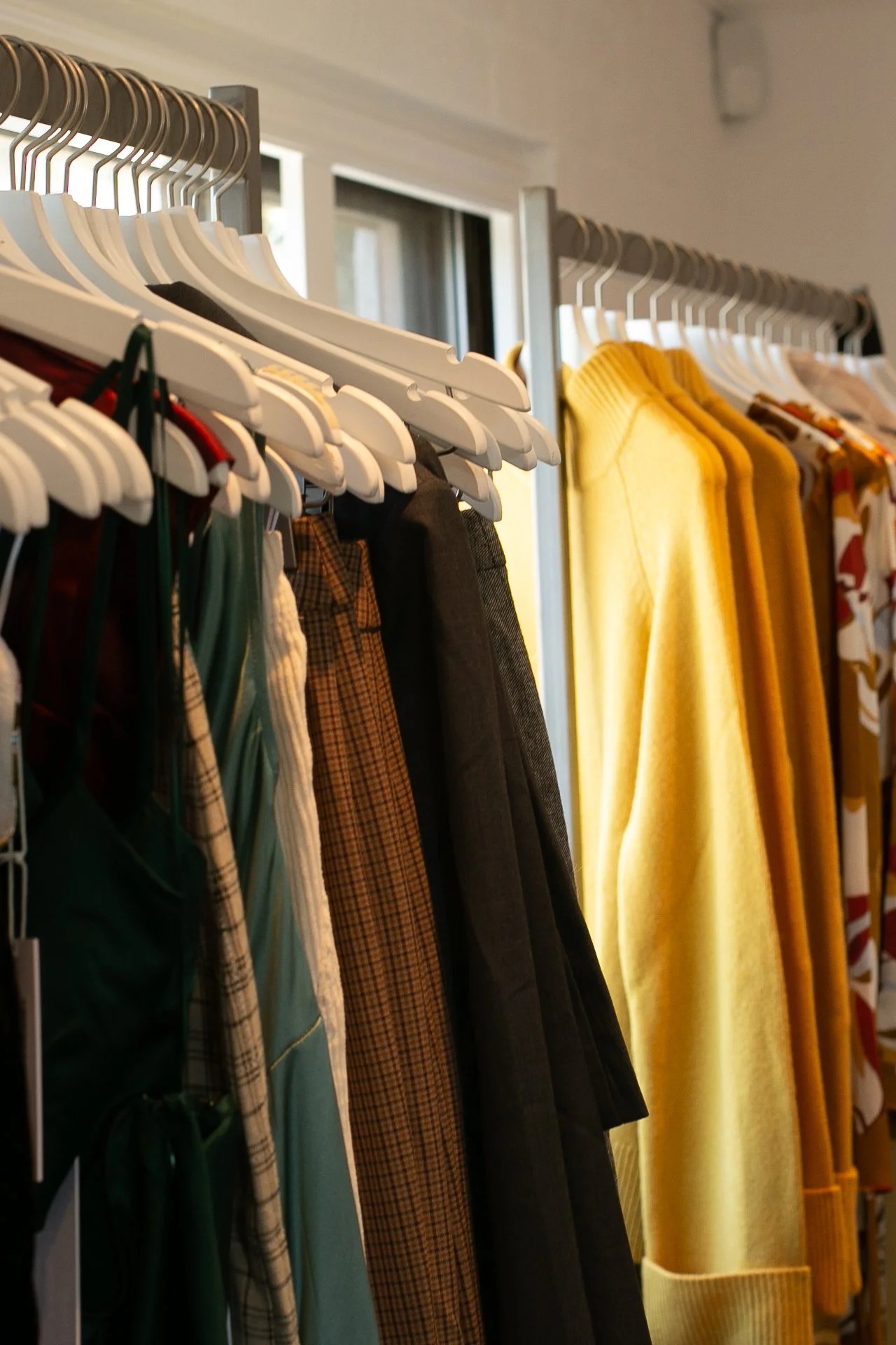 Clothing in muted tones and yellow hanging on white hangers in The A List showroom