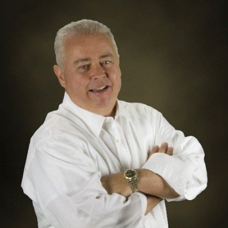 The Assurance Group founder Ed Shackelford in a white shirt, standing with his arms folded