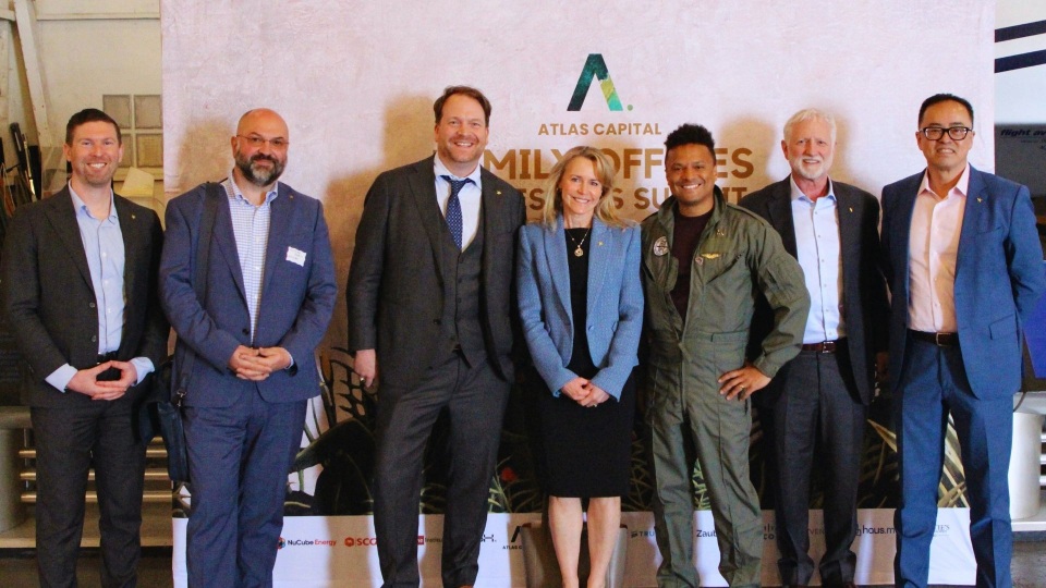 Seven attendees posing in front of an Atlas Capital Family Offices and Investors Summit backdrop