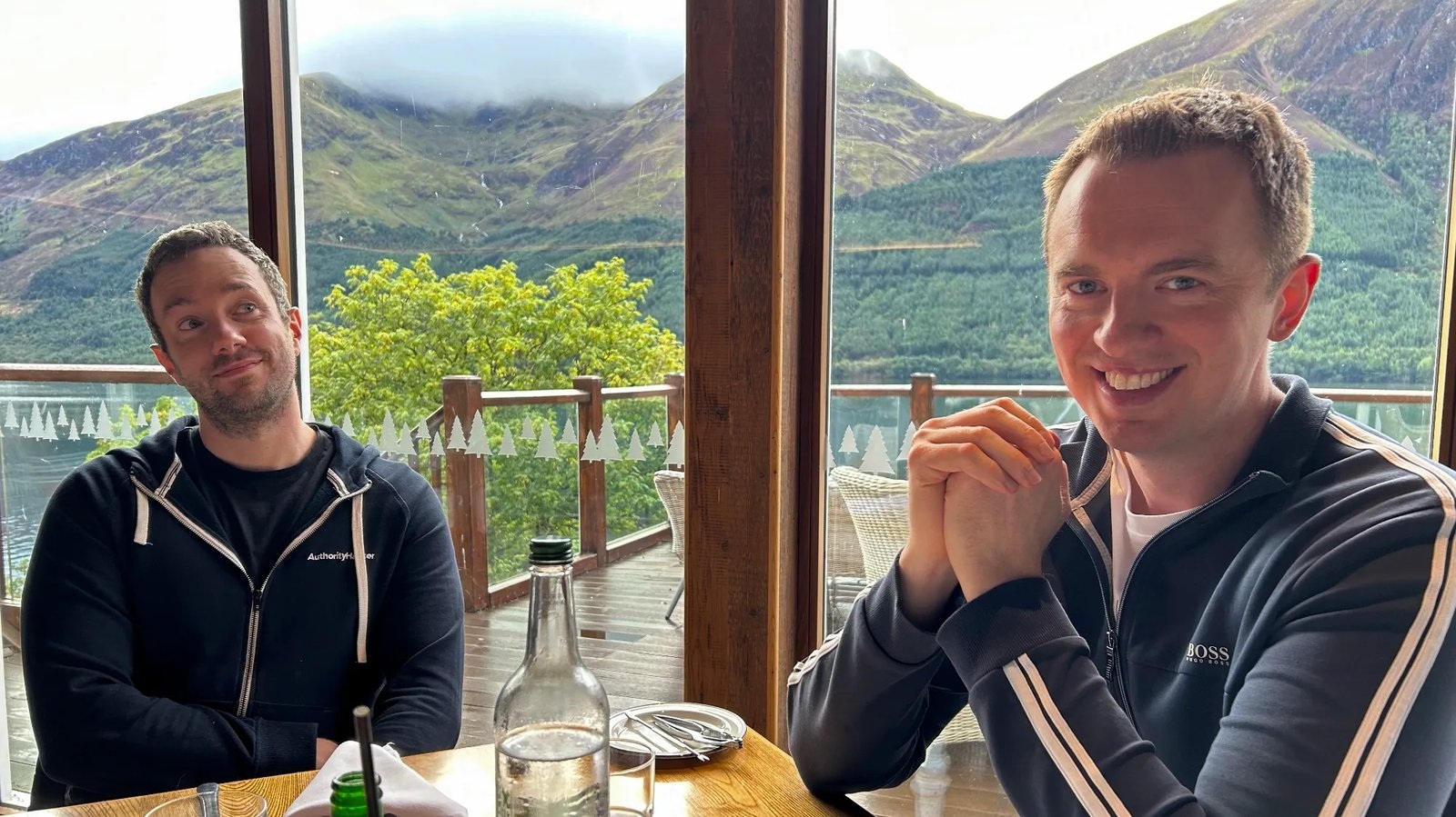 Gael Breton and Mark Webster sitting at a table beside windows overlooking green mountains