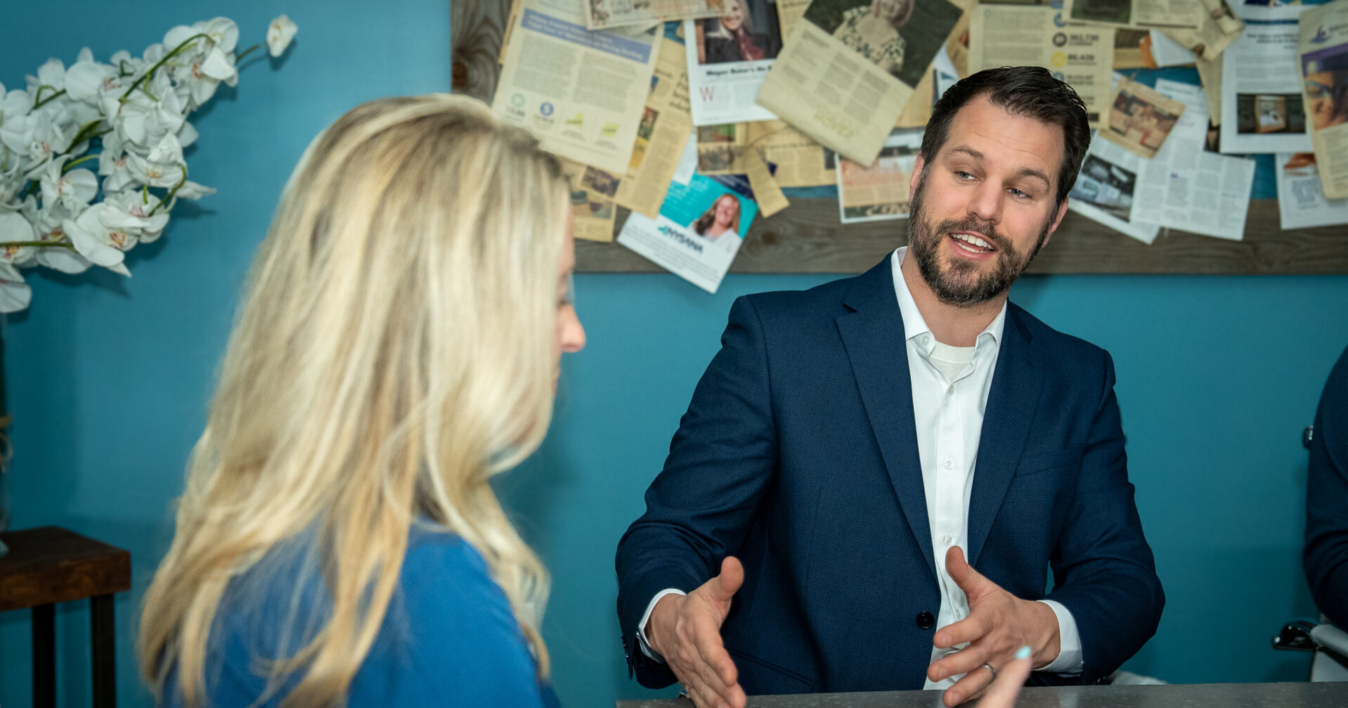 Two people in discussion at The Baker Agency office with press clippings behind them