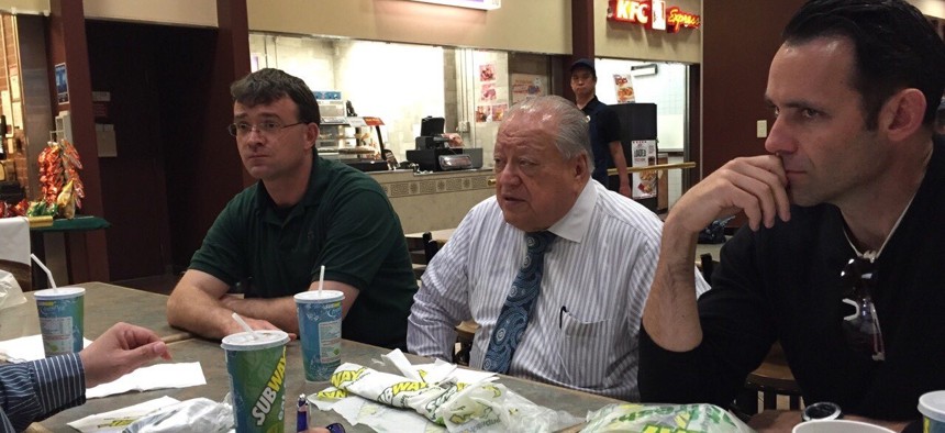 Fernando Galaviz sits at the center of a business meeting in a food court, with documents and sandwich wrappers on the table.