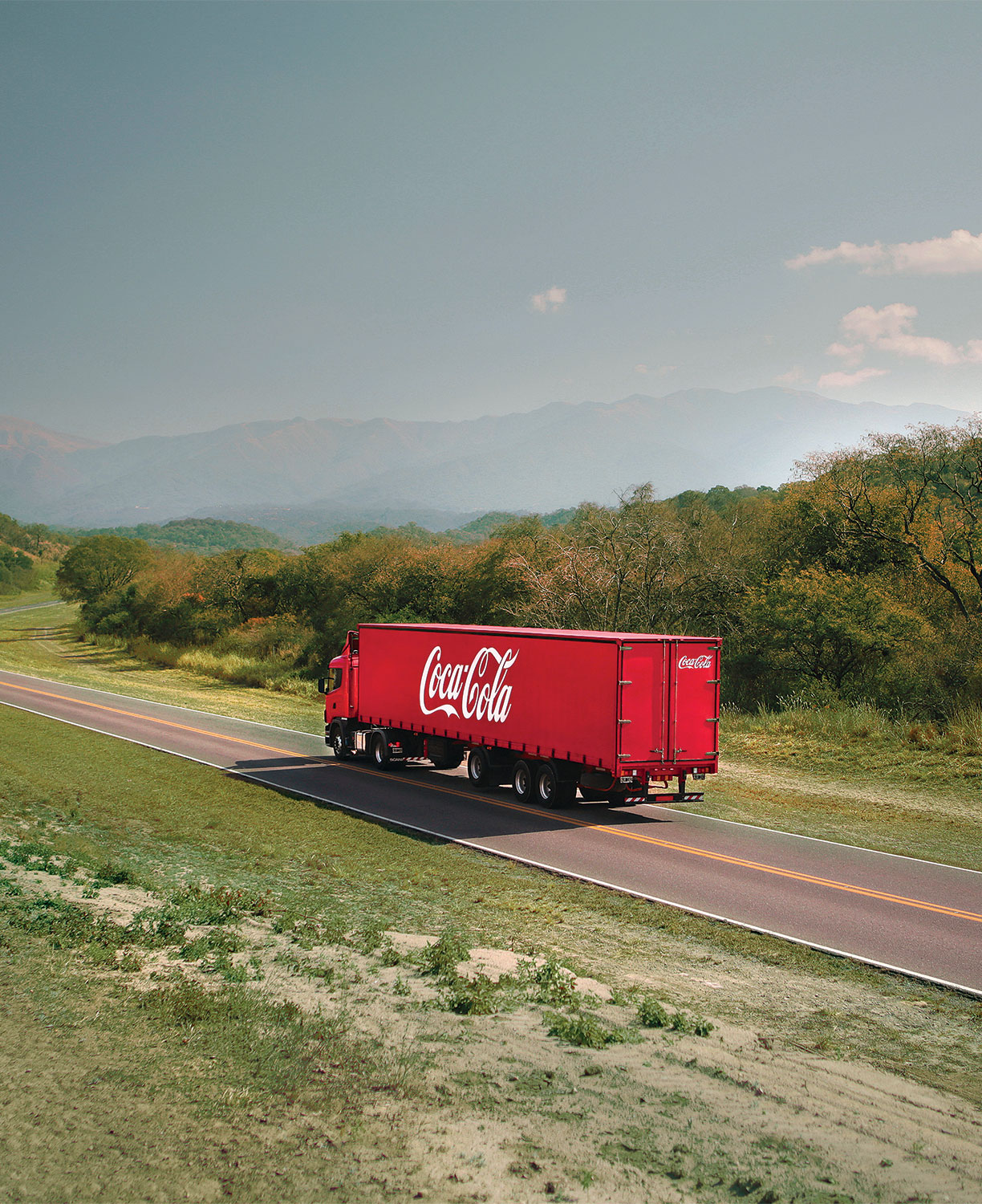A red Coca-Cola delivery truck traveling along a rural road