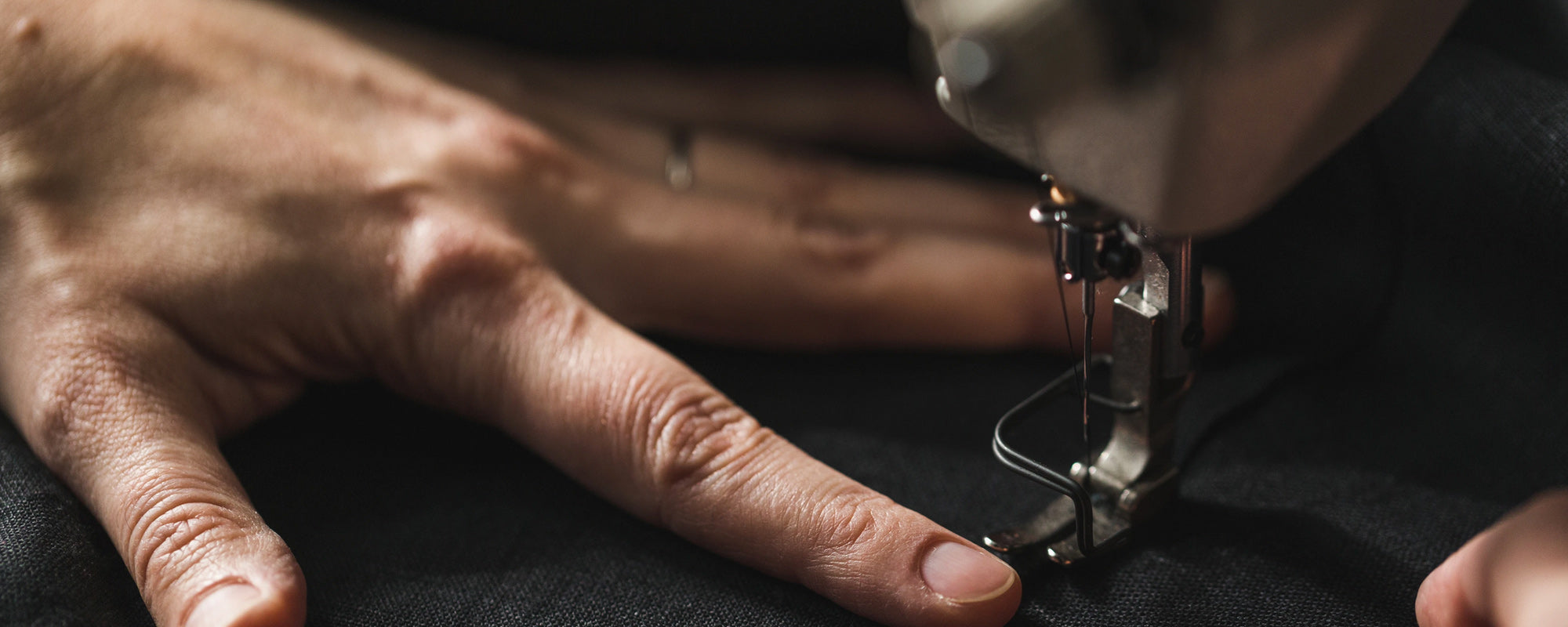 Close-up of hands guiding cloth beneath a sewing-machine needle
