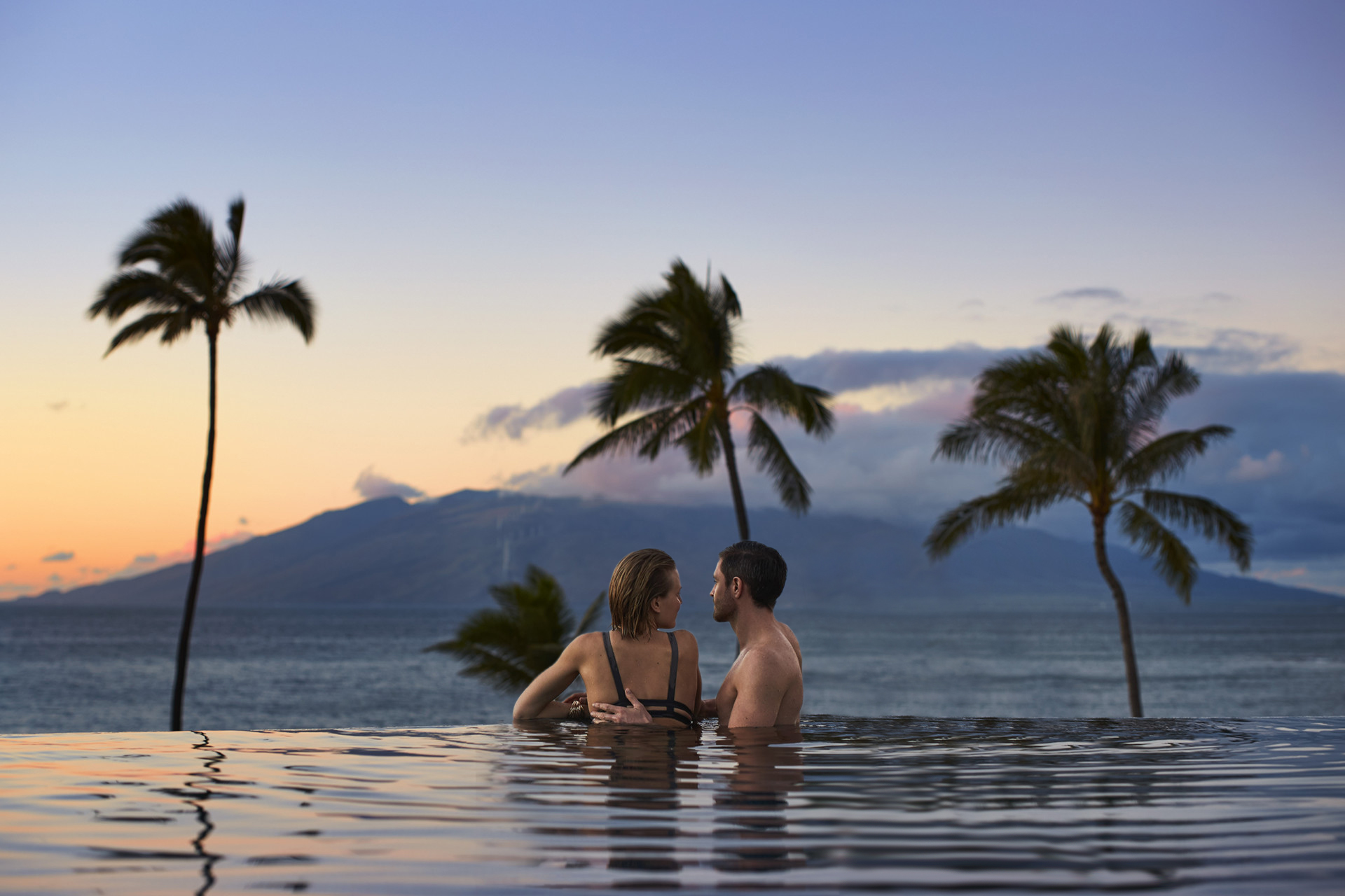 Guests in an infinity pool overlooking Maui at sunset