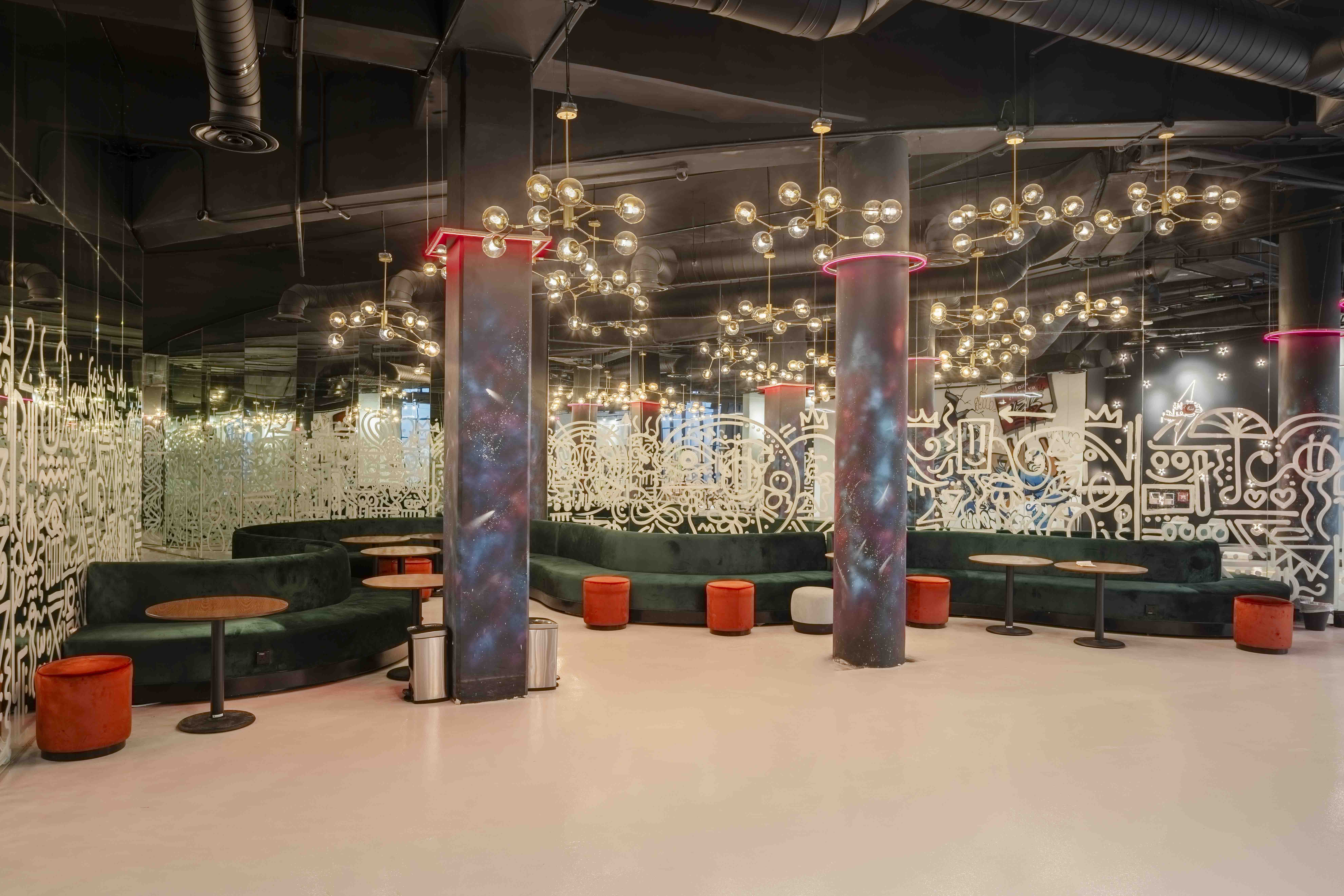 The Garage lounge with exposed concrete columns, illuminated glass walls and curved green seating
