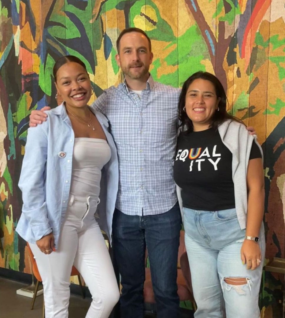 Three people pictured in The Lacek Group’s culture photography, standing before a colorful mural
