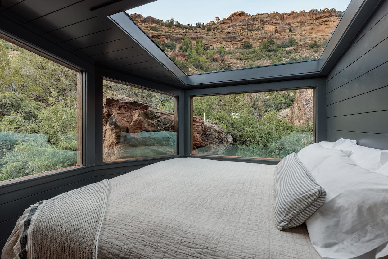 A bed beneath a large skylight at Open Sky Zion, with canyon rock visible through the windows