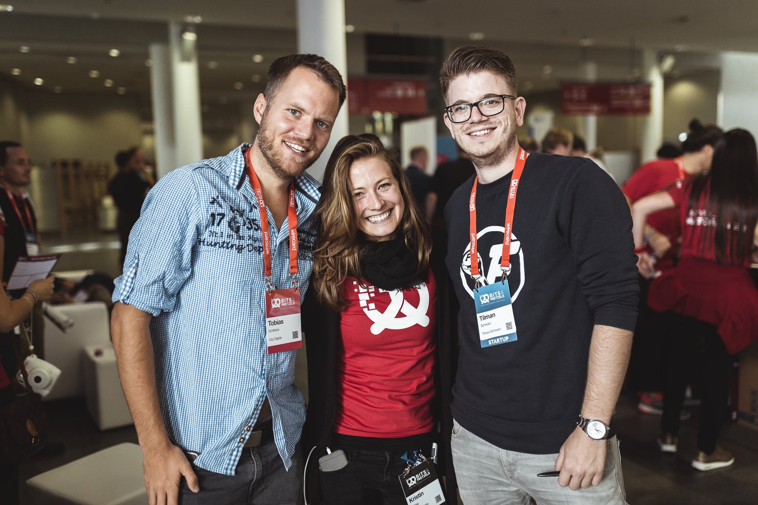 Three people smiling at Bits and Pretzels, with a red-shirted matchmaker in the middle