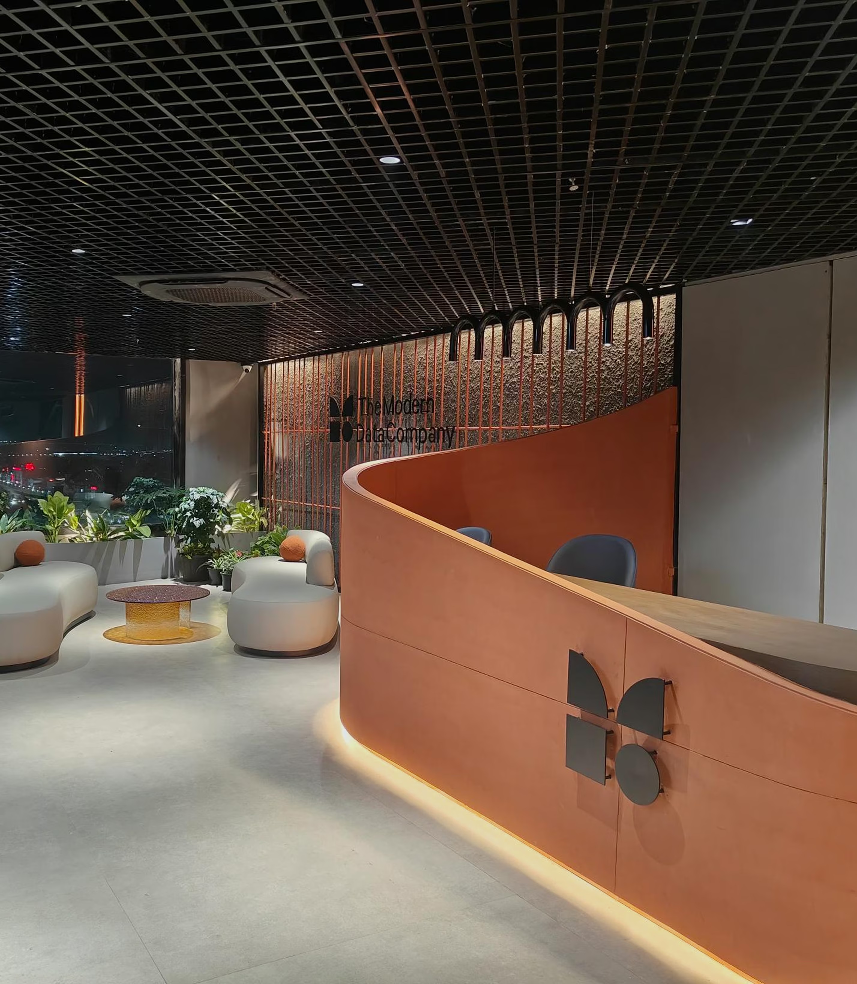 Modern’s office reception with a curved orange desk, lounge chairs, plants, and a gridded ceiling