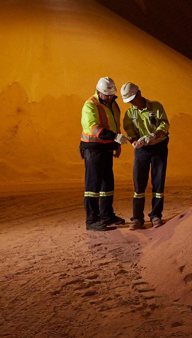 Two Mosaic workers in hard hats examine material in a mine