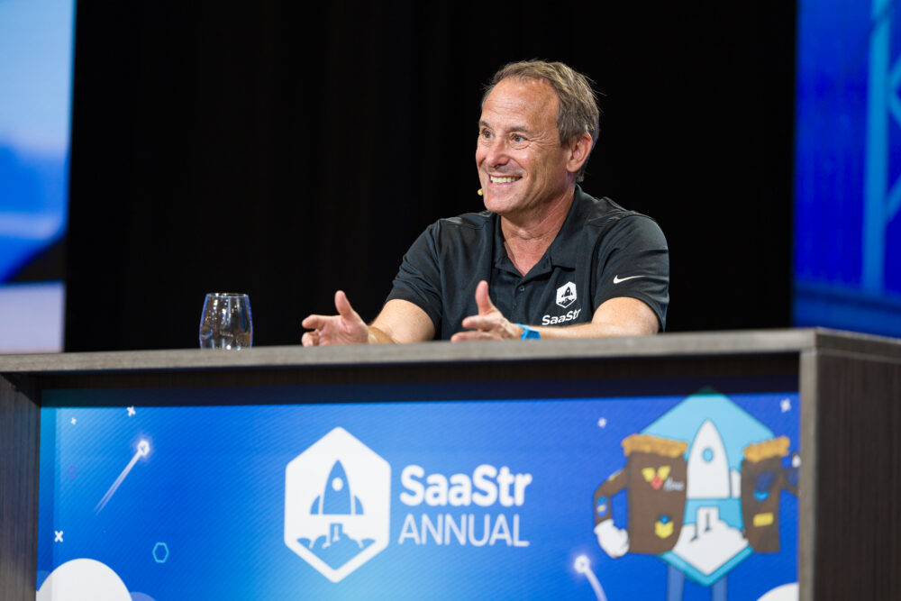 Jason Lemkin speaking from a desk on the SaaStr Annual stage