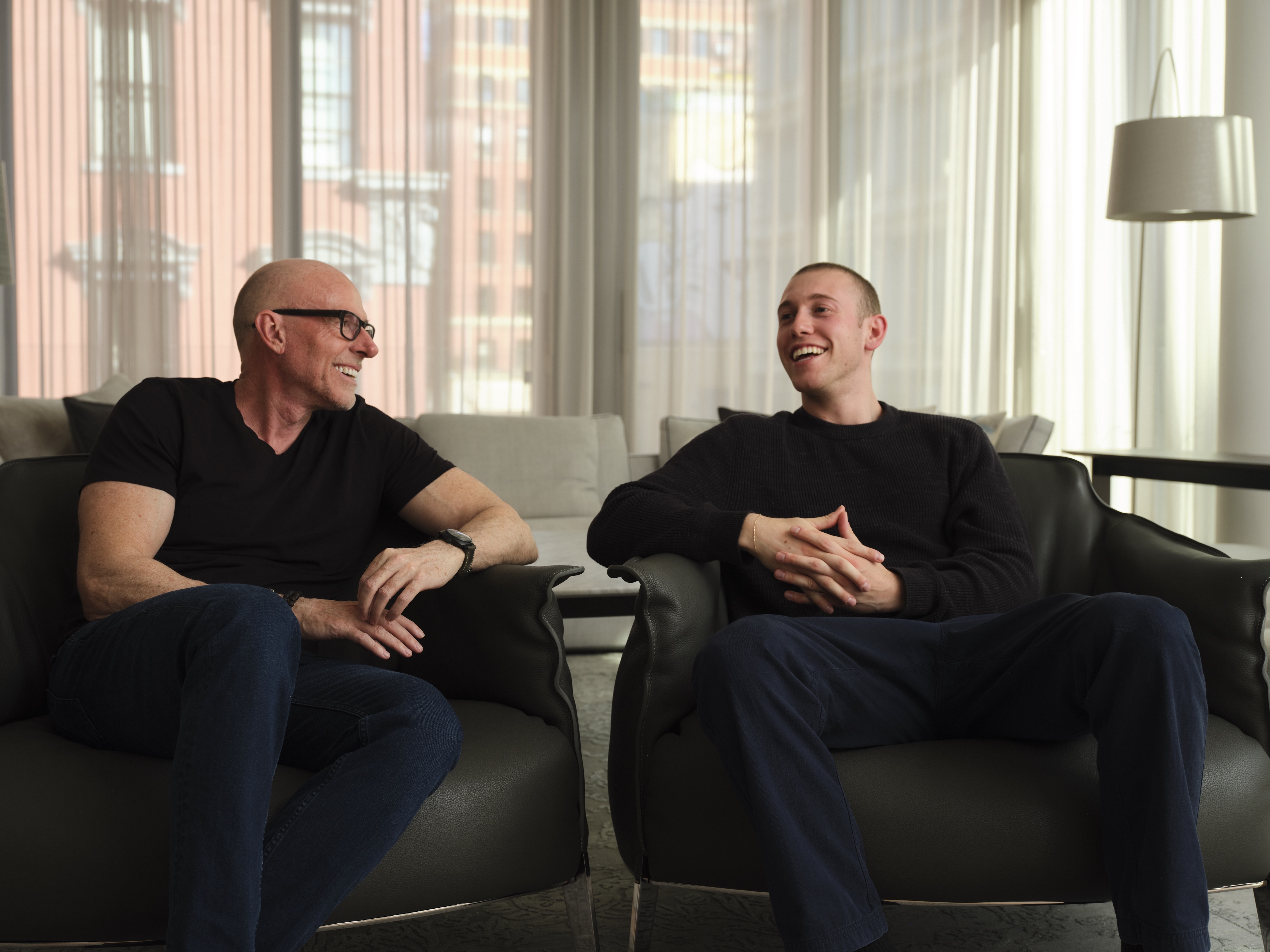 Scott Galloway, left, and Ed Elson laughing while seated in armchairs