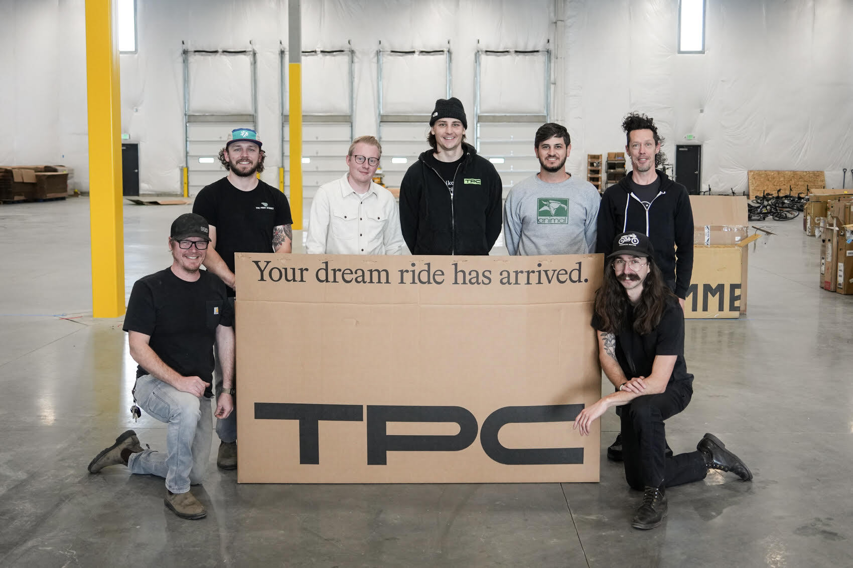 Returning TPC team gathered behind a bike shipping box in the Thornton warehouse