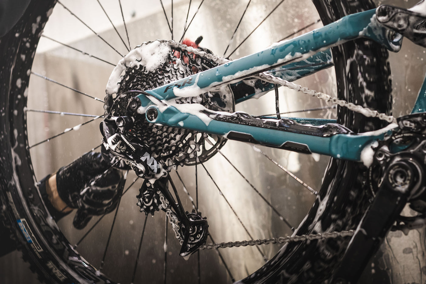 A mechanic washing a turquoise bicycle drivetrain