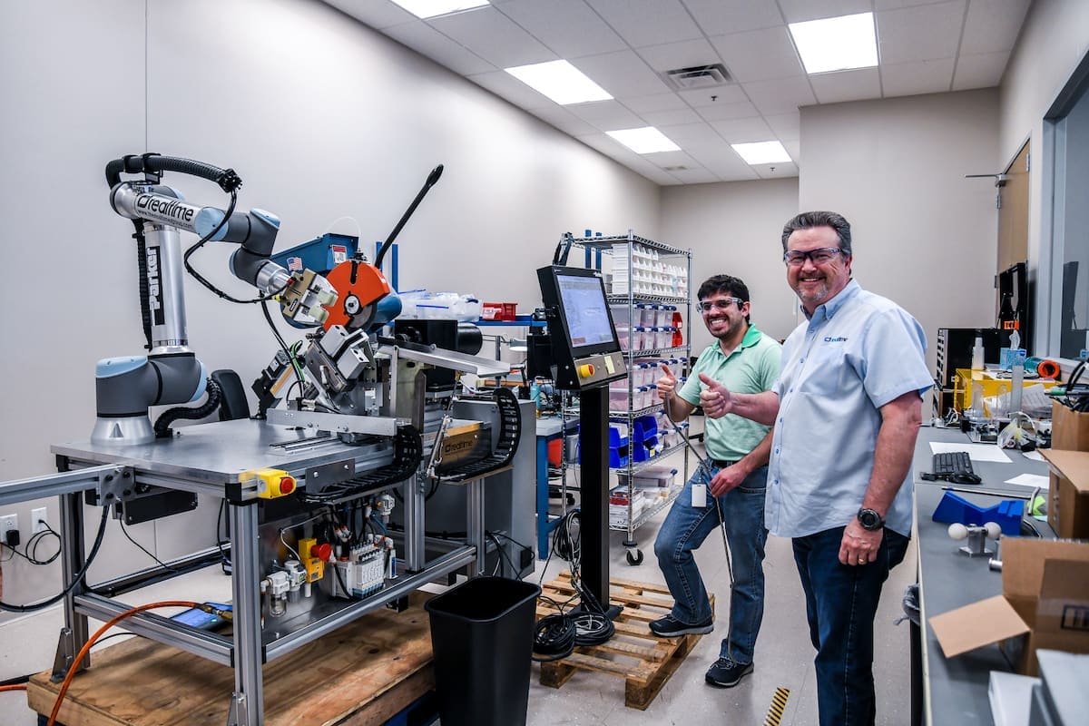 Two Realtime team members beside robotic equipment in an engineering workspace