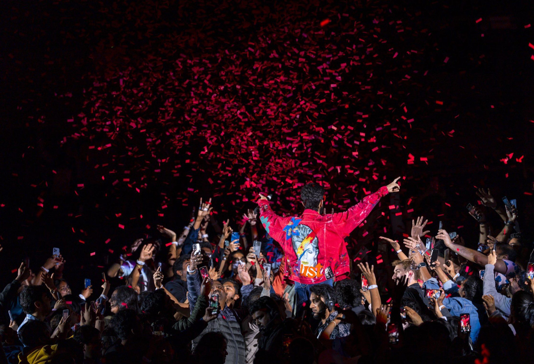 A packed arena crowd under confetti during a South Asian live music tour