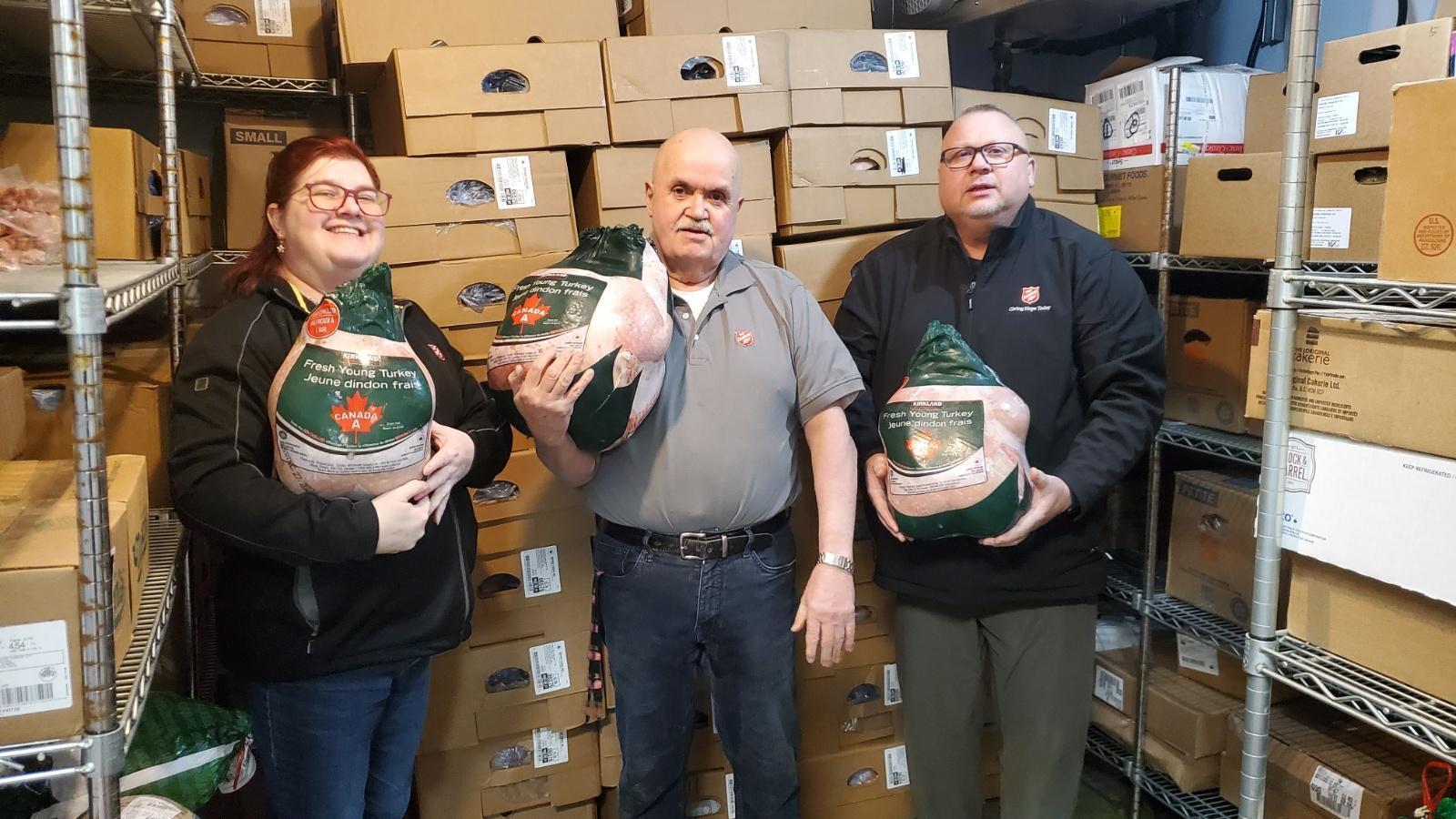 Three Salvation Army and Costco staff members hold frozen turkeys in a Grande Prairie food bank storeroom