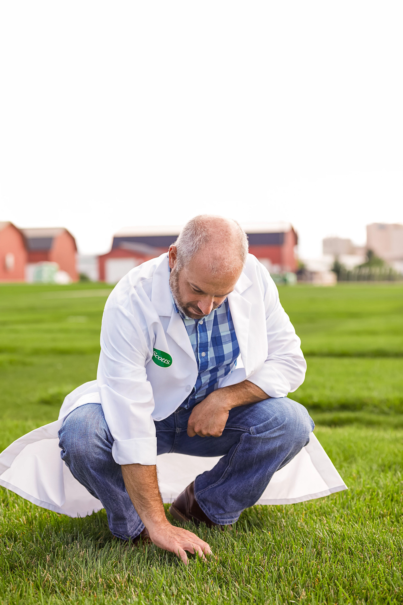 A Scotts researcher in a white coat examining turf outdoors