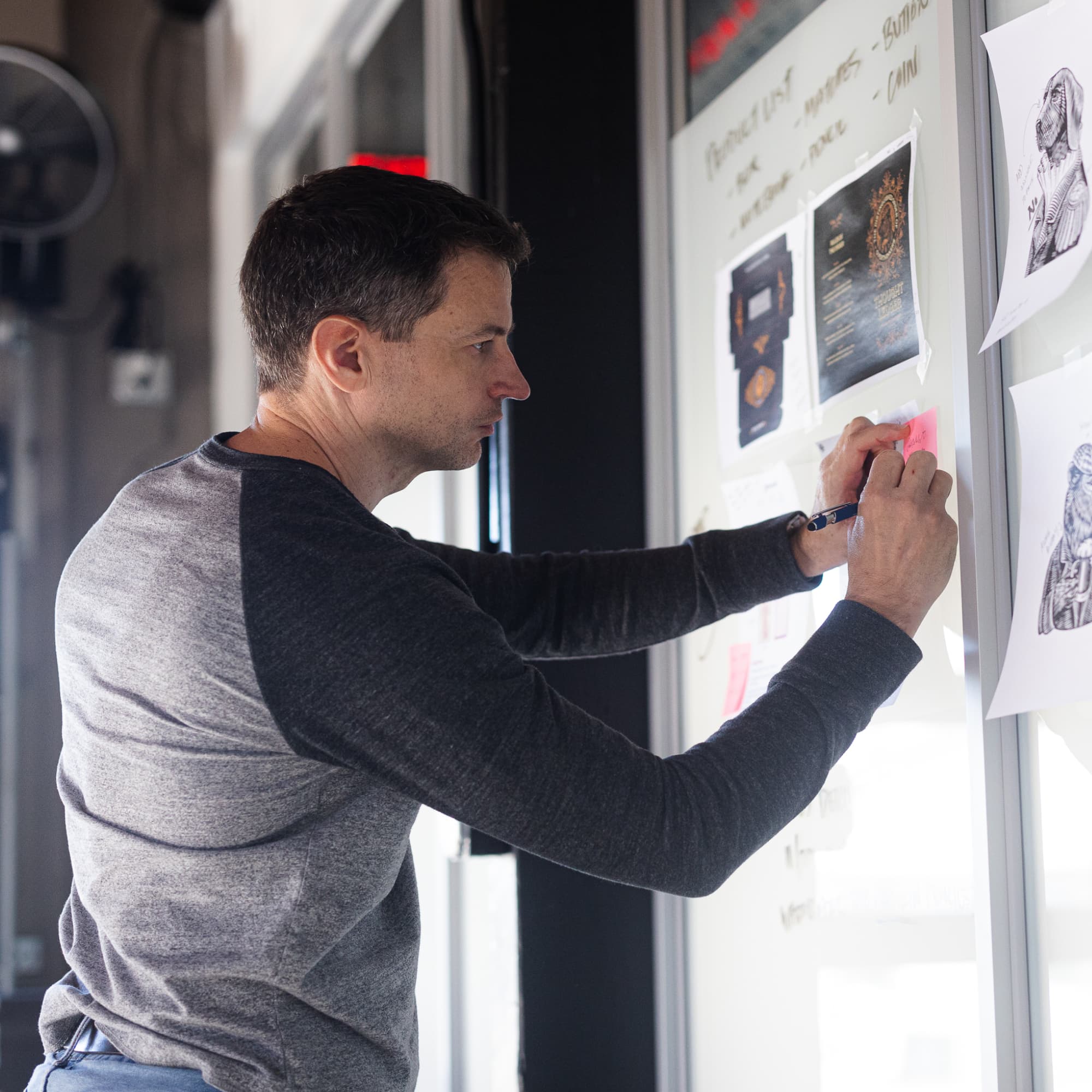 A Taproot Agency team member reviews printed design concepts and sticky notes on a wall