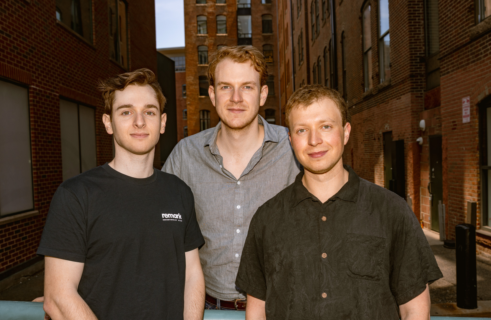Remark co-founders Theo Satloff, Ian Patterson and Carl-Philip Majgaard standing together between brick buildings